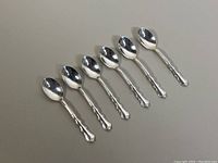 Six 4-inch sterling silver coffee spoons arranged on neutral surface showing detailed handles and spoon bowls.