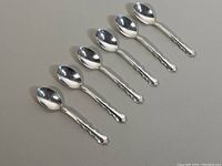 Six silver coffee spoons aligned side by side on a light background showing full length and design detail