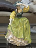 Front view of Royal Doulton Buttercup porcelain figurine in green and yellow dress holding a hat.