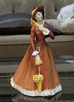 Front view of Royal Doulton Julia HN 2705 porcelain figurine showing figure in orange-brown dress with yellow umbrella.