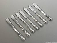 Seven sterling silver handled spreader knives laid out, showing handles and blades in full view.