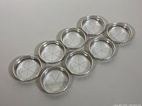 Eight circular coasters arranged on a flat surface, top view showing smooth silver rims and clear crystal bases with starburst pattern.