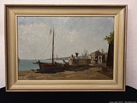 Framed oil painting showing entire harbor scene with figures and boats, in a cream-colored frame on display.