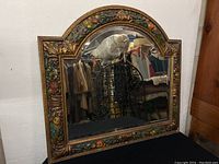 Front view of the antique wall mirror showing full carved frame and reflection of some coats in the background