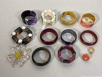 Overall lot showing various bangles, bracelets, rings, and a Lucite yellow daisy flower brooch arranged on a grey surface.
