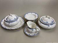 Overview of the dish set showing two covered serving dishes on under-plates, eight cereal bowls stacked, the gravy boat with under-plate, all with blue floral pattern and gold trim