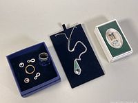 All items presented in their display boxes including rings, earrings, necklace, and miniature flip mobile phone