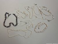 Overview photo displaying all six pearl necklaces laid flat on a gray surface to show variety in bead size and color.