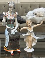 Photo showing both porcelain figurines on a glass table with a sofa and dog in the background, highlighting scale and condition.