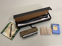 Full lot with black Xaphoon pocket saxophone in original box, green instruction manual, M. Suzuki Humming Pipe-Harmonica with soft tan case, clarinet reeds in original boxes and sleeves.
