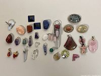Full overview of all 26 semi precious stone pendants laid out on a surface showing variety of stones, shapes and sizes.