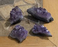 Four raw amethyst crystal pieces showing purple crystalline structures on gray bases placed on a flat surface.