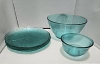 Photo showing 2 blue glass serving bowls and 4 blue glass plates stacked beside them.