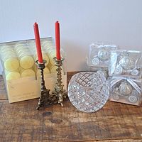 Fragrant yellow tea lights, brass candlesticks with red candles, Cinderella carriage candle holders in packaging, and crystal patterned glass candle holder on wooden surface.