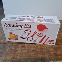 Box of new 6-piece canning set for jars, showing included utensils in red and metal for making ketchup, strawberry jam.