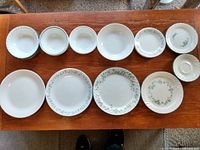 Top view of 11 plates with different floral vine patterns and plain white design, arranged on wooden surface