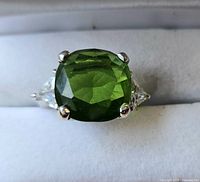 Front-facing close-up of the ring showing the large green gemstone and side clear stones.