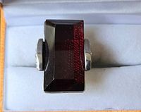 Front view of the fashion ring showing large rectangular deep red stone set in silver-tone band.