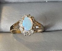 Top view of gold ring featuring oval opal center stone and diamond halo, displayed in ring box.