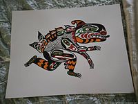 Photo of the unsigned print titled 'Sea Monster' showing bold Indigenous art style with black, orange, green, and red patterns on white paper.