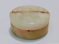 Closed view of small round onyx stone pillbox showing creamy white color with brown veining and polished smooth finish.