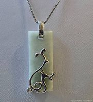 Close-up of the rectangular pendant with silver ornate design showing details of the overlay and bail connecting to the chain.