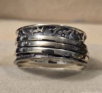 Front view of the sterling silver spinner ring showing floral pattern on fixed band and three smooth spinner bands.