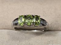 Front view of the sterling silver ring showing three oval Arizona peridot stones and sets of small white zircon stones along the band.