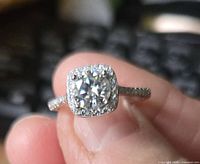 Close-up photo of the sterling silver ring held between fingers, showcasing the central round moissanite stone with square halo of smaller stones on band.