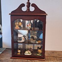 Front view of the vintage wooden curio cabinet with glass door and mirrored back showing small decorative figurines inside.