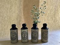 Four antique stoneware ginger beer bottles with deep blue glazed tops, off-white bodies and black transfer stamped North & Randall Aylesbury ginger beer logos. One bottle contains small white flowers for display.