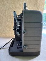 Side view of the Bell & Howell Model 253-AR 8MM film projector showing the textured metal casing, projection lens, and adjustment knobs.