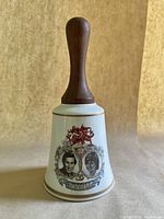 Full view of the porcelain and wood commemorative wedding bell featuring the printed images of Prince Charles and Lady Diana Spencer and Welsh dragon emblem.
