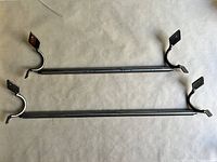 Photo showing both blackened metal towel bars laid flat, highlighting the full length and the mounting brackets at each end.