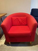 Front view of one red fabric bucket-style chair with wooden legs and a red pillow placed inside the chair.