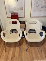 Front view of two white Umbra Oh Chairs placed on a hardwood floor, showing seat and backrest design with armrests.