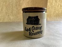 Front view of the ceramic canister showing the log cabin graphic and 'Log Cabin Remedies' text.