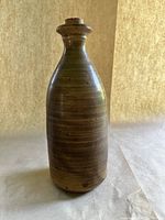 Front angle view of vintage stoneware jug, showing narrow neck, cork stopper in place, and earthy matte finish with horizontal striations