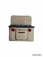 Front and angled view of vintage white and blue tin toy stove showing red knobs and handle, backsplash, and surface wear including rust and scratches.