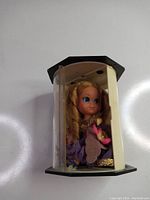 Front angled view of 1967 Mattel Liddel Kiddle Doll in original hexagonal display packaging showing doll with blonde curly hair, blue eyes, and detailed dress.