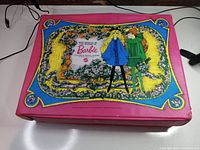Front and top view of the pink 1968 Barbie carrying case with illustrated fabric top featuring two Barbie dolls and floral design.