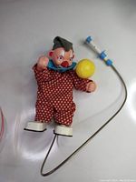 Full view of the vintage clown toy in red and white polka dot outfit holding a yellow ball with connected wired remote control with blue push button.