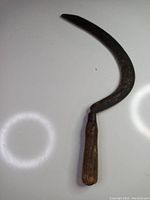 Side view of antique hand sickle showing curved, rusted metal blade and wooden handle.