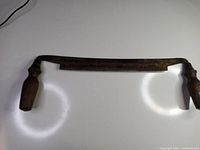 Front view of antique manual tree bark stripper showing curved metal blade and wooden handles