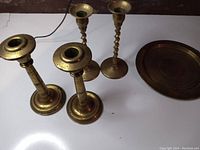 Four brass candlesticks and one round brass plate displayed on a white surface, showing overall items in the lot.