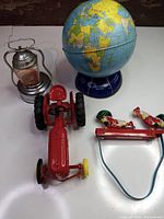 Photo showing all four collectible toys together: Ohio Art tin lithograph globe, AAA miniature lantern, Massey Harris red tractor toy, and reproduction clucking rooster litho toy.