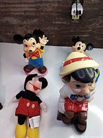 Photo showing all four Disney collectibles including ceramic Pinocchio, stuffed Mickey Mouse, vintage figurine and dog/cat bowl.