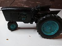 Side view of the hand-painted black tractor with teal wheels and engine details, showing the tires, exhaust, and vents.