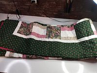 Quilt folded showing dark green and floral patchwork squares with white border and quilting stitches.