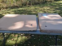 Two large flat-packed cardboard boxes placed on an outdoor table in sunlight